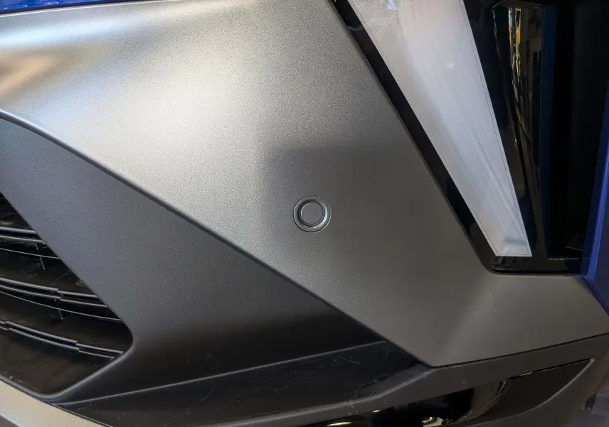 Détail du pare-chocs avant gris mat avec capteur de stationnement sur Renault Captur E-Tech bleu Iron toit noir.
