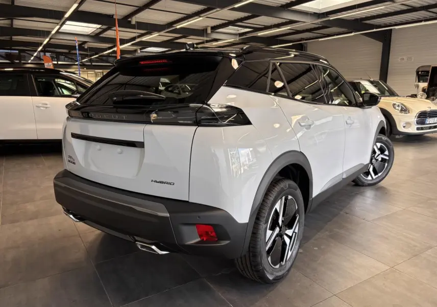 Vue 3/4 arrière droite d'un Peugeot 2008 blanc hybride 2025 avec toit noir et jantes distinctives en concession.