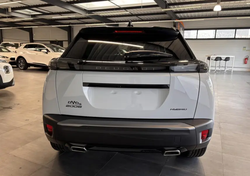 Vue arrière d'un Peugeot 2008 blanc hybride 2025 en intérieur, avec double sortie d'échappement et vitrage teinté noir.
