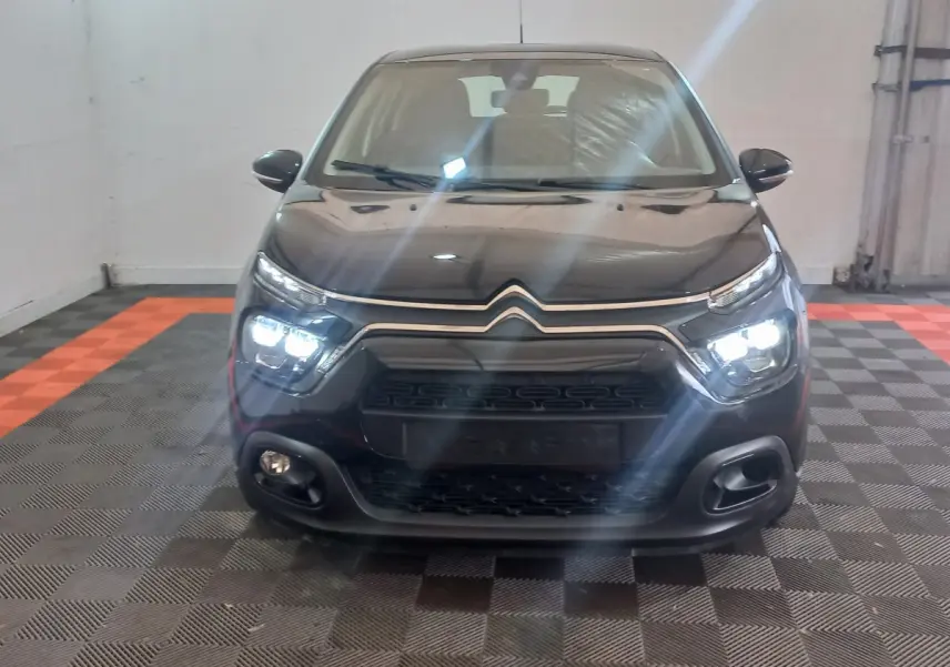 Vue avant d'une Citroën C3 noire 2024 avec phares LED allumés dans un garage au sol damier noir et orange.