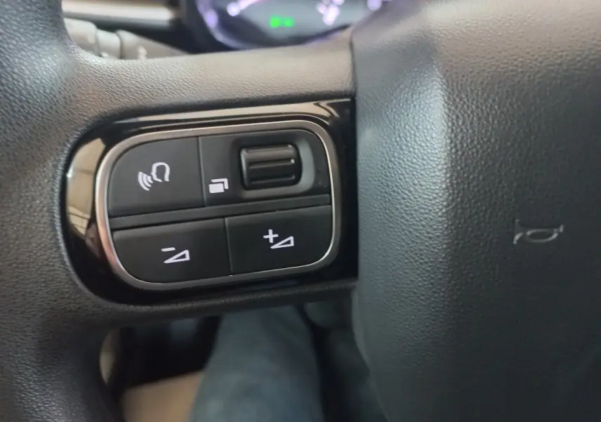 Gros plan sur les commandes vocales et volume du volant noir de la Citroën C3 BlueHDi 2024.