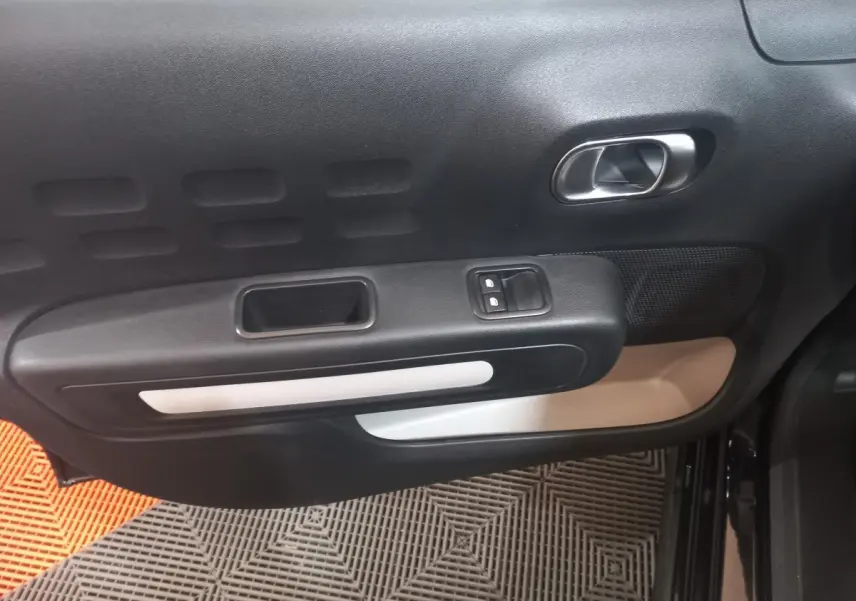 Vue rapprochée de la porte intérieure côté gauche de la Citroën C3 noire, avec poignée argentée et commandes de fenêtre.