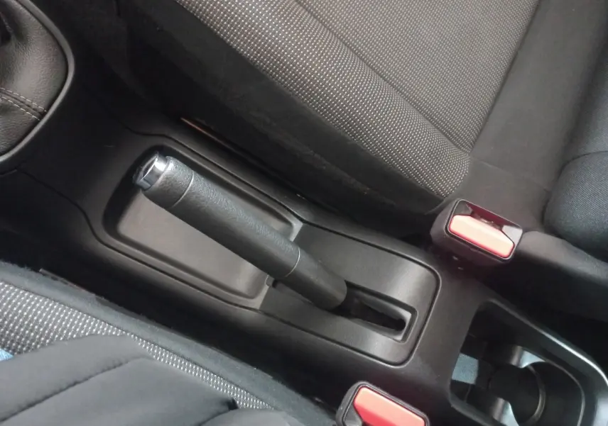 Vue rapprochée de la poignée de frein à main noir et des ceintures de sécurité rouges dans l’habitacle d’une Citroën C3 noire.