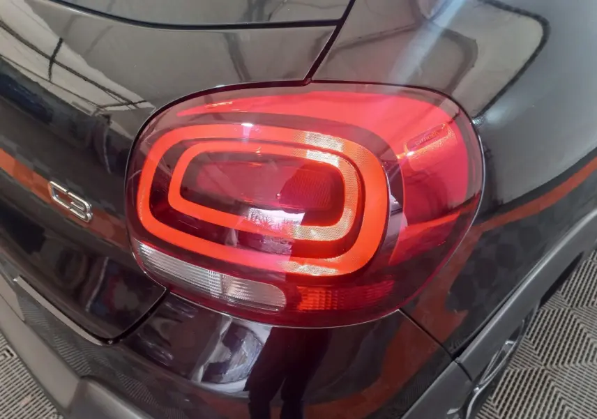 Gros plan sur le feu arrière droit rouge et le logo C3 d'une Citroën C3 noire 2024 vue de l'arrière.