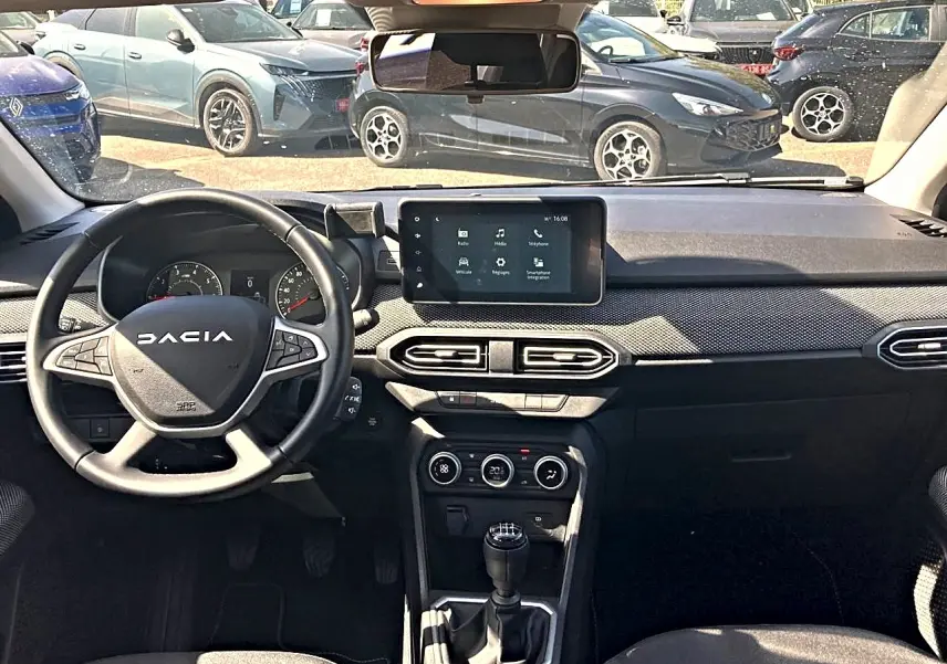 Vue intérieure avant du tableau de bord noir de la Dacia Sandero 2025 avec volant multifonctions et écran tactile central.