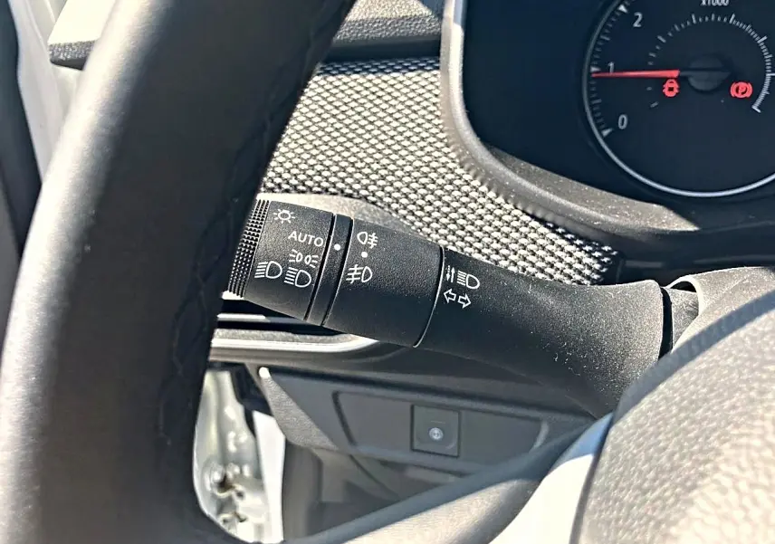 Gros plan sur la commande des feux et clignotants à gauche du volant dans l’habitacle d’une Dacia Sandero blanche.