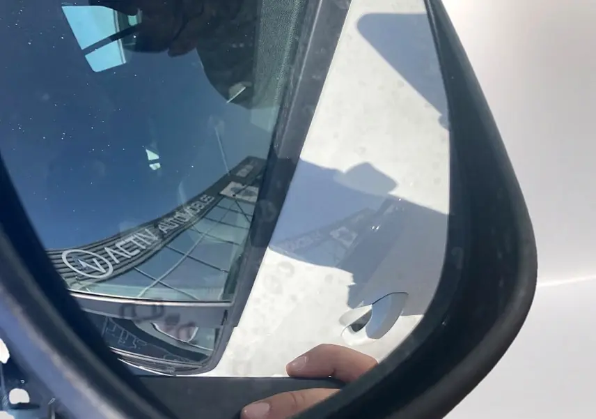 Rétroviseur côté droit montrant une Dacia Sandero blanche avec reflet d’un bâtiment et main sur la portière.