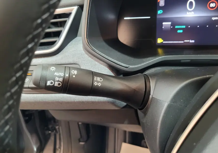 Gros plan sur la commande des feux à gauche du volant dans l'habitacle gris foncé de la Renault Clio 2025.