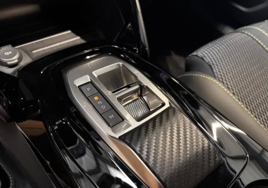 Gros plan sur la console centrale du Peugeot 2008 gris, mettant en valeur la boîte automatique et les surpiqûres vertes des sièges.