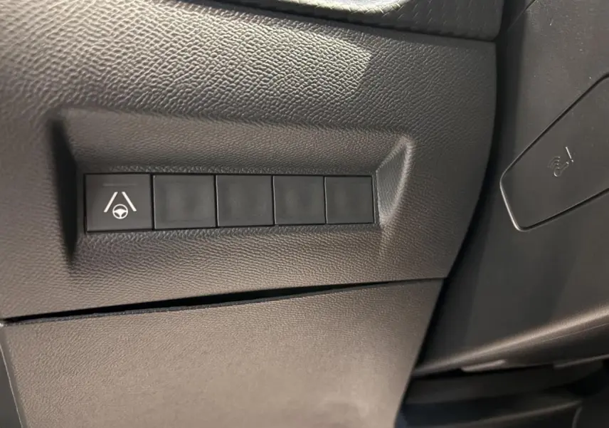 Gros plan sur les boutons de commande en plastique noir sur la partie inférieure gauche du tableau de bord du Peugeot 2008 gris.