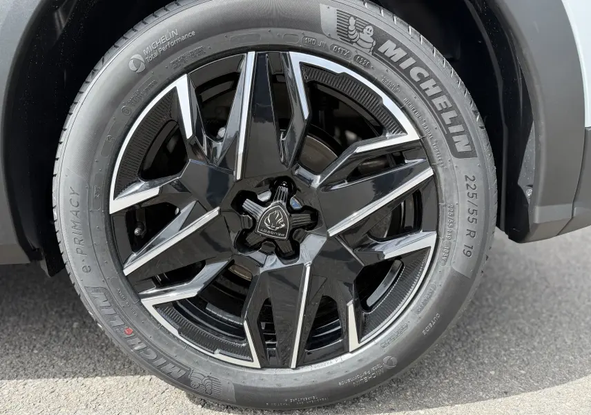Gros plan sur la roue avant droite du Peugeot 3008 Hybrid blanc Okenite avec jante noire brillante et logo Peugeot central.