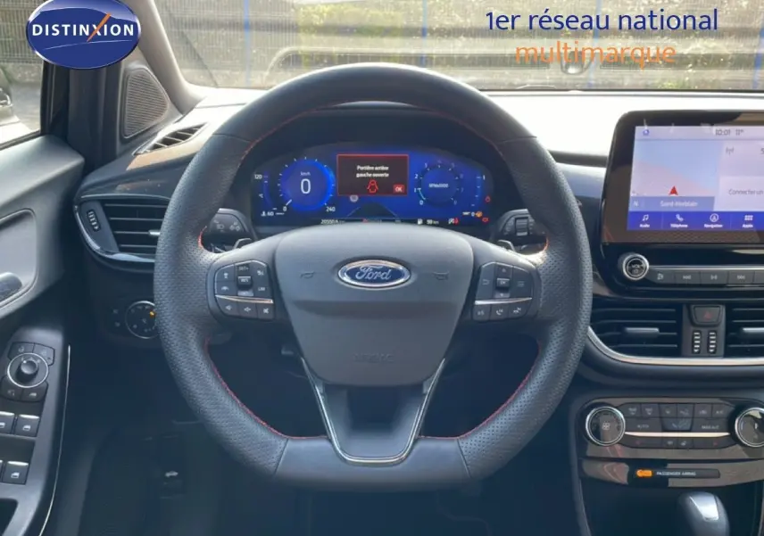 Vue intérieure centrée sur le volant noir avec surpiqûres rouges et tableau de bord numérique du Ford Puma 2023.