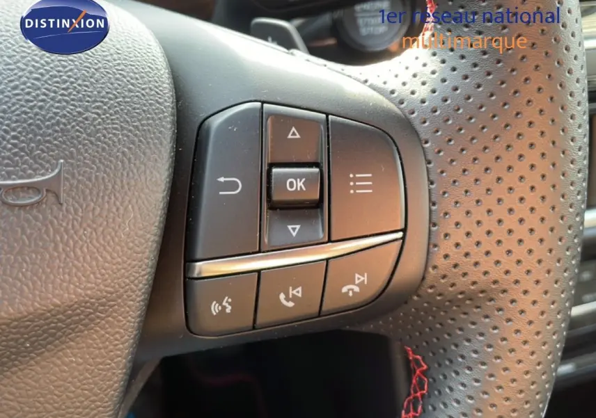 Gros plan sur les commandes au volant en cuir perforé noir avec surpiqûres rouges du Ford Puma noir Agate 2023.