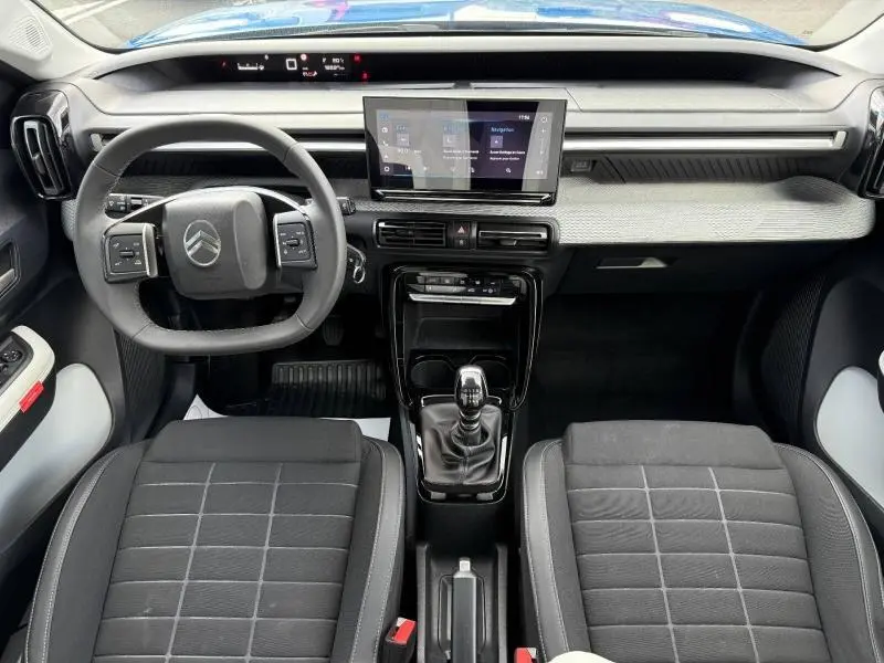 Vue intérieure avant du tableau de bord et volant de la Citroën C3 2025 avec écran tactile et sièges noirs.