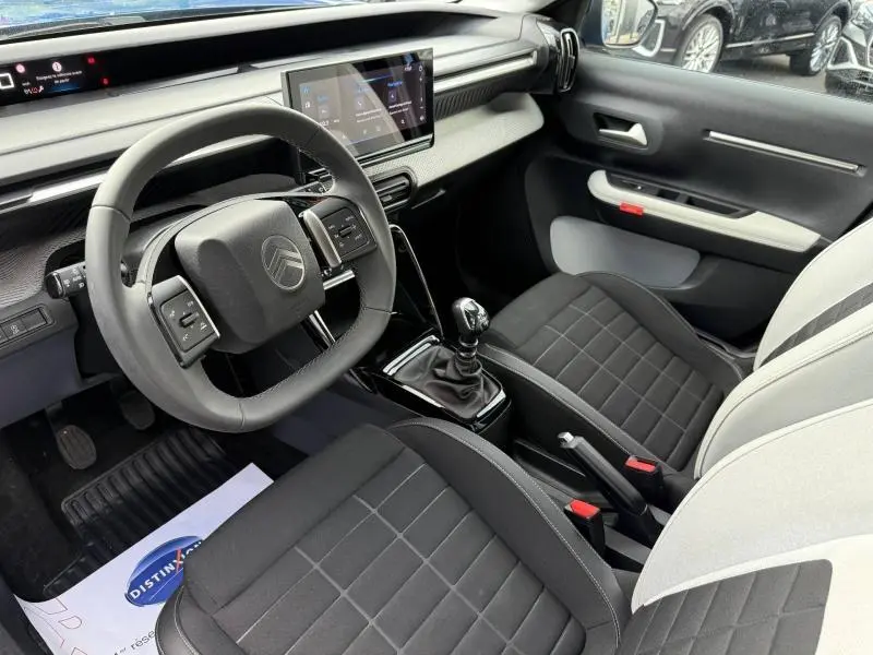 Vue intérieure avant droite de la Citroën C3 2025 avec volant multifonction, sièges bicolores et écran tactile central.