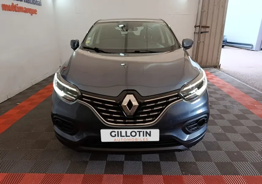 Vue frontale d'un Renault Kadjar Business gris foncé avec calandre chromée et phares LED allumés dans un showroom.