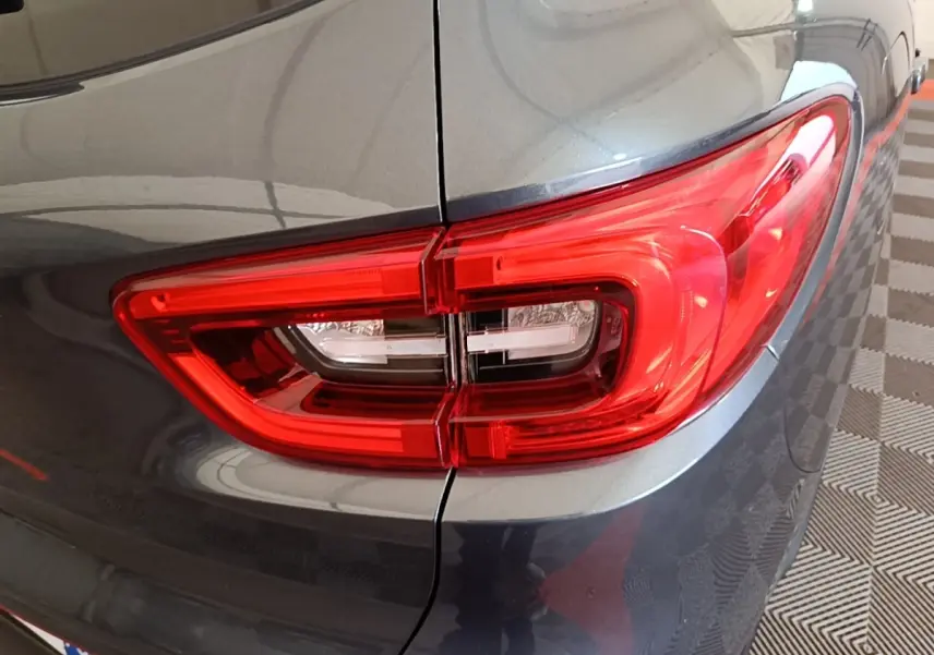 Gros plan sur le feu arrière droit rouge d’un Renault Kadjar gris foncé, avec reflet sur la carrosserie lisse.