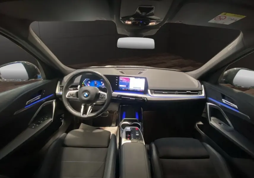 Vue intérieure avant du BMW X1 2025 noir, avec tableau de bord digital et éclairage d'ambiance bleu subtil.