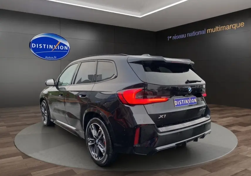 BMW X1 noir vue 3/4 arrière droite, avec feux LED allumés et jantes alliage distinctives.