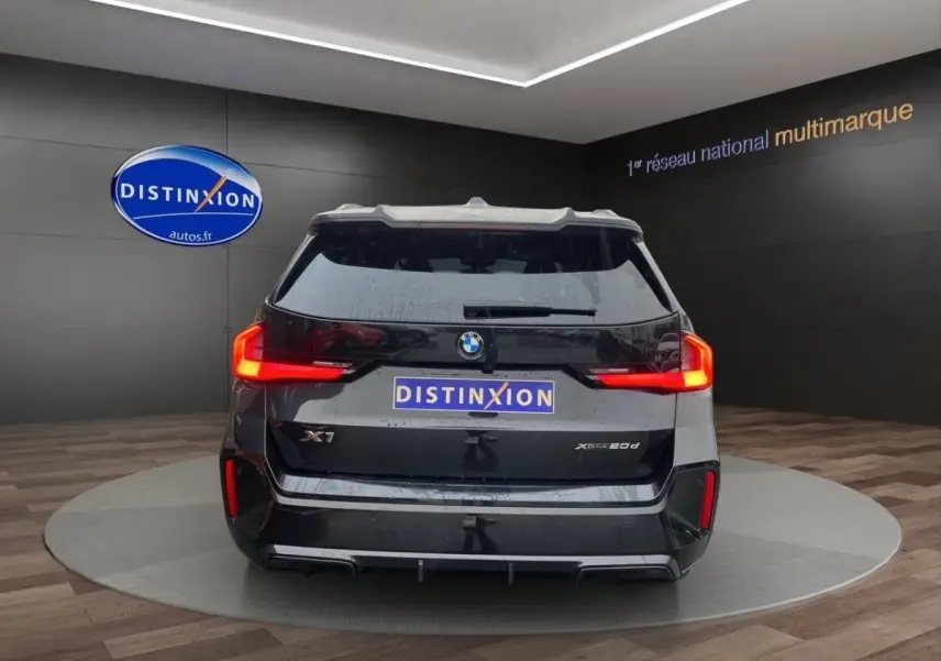 Vue arrière d’un BMW X1 noir 2025 avec feux LED distinctifs et logo xDrive20d sur fond showroom.
