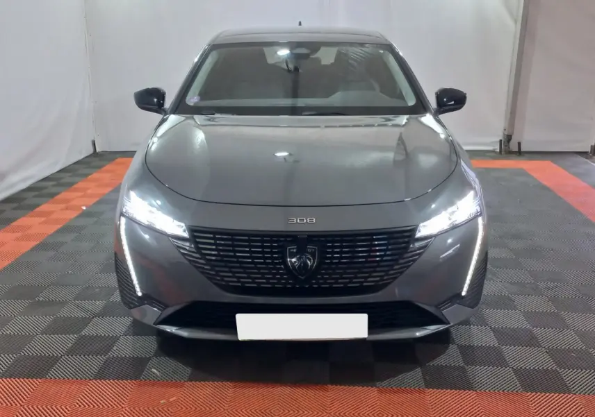 Vue frontale d'une Peugeot 308 PHEV 180 E-EAT8 Allure gris foncé avec phares LED allumés dans un garage.