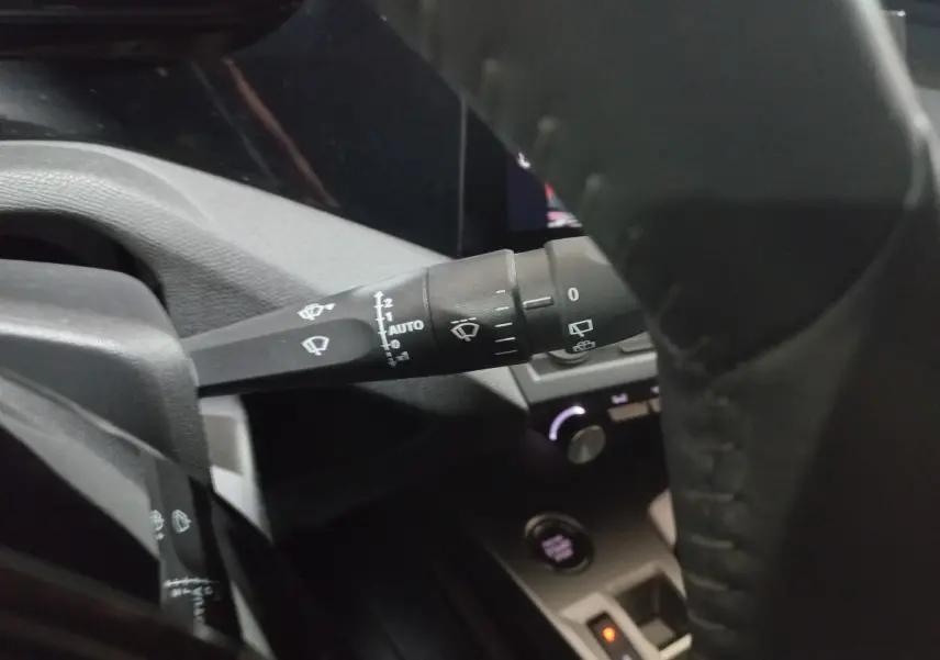 Gros plan sur la manette d’essuie-glace à gauche du volant cuir dans l’habitacle sombre d’une Peugeot 308 PHEV 2025.