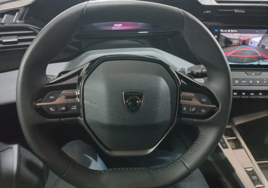 Vue rapprochée du volant cuir multifonctions Peugeot 308 PHEV 2025 avec tableau de bord numérique et écran de caméra de recul.
