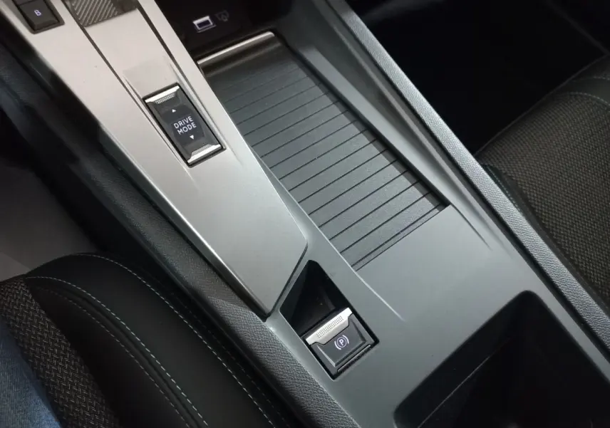 Gros plan sur la console centrale grise avec bouton Drive Mode et frein à main électrique dans Peugeot 308 PHEV 2025.
