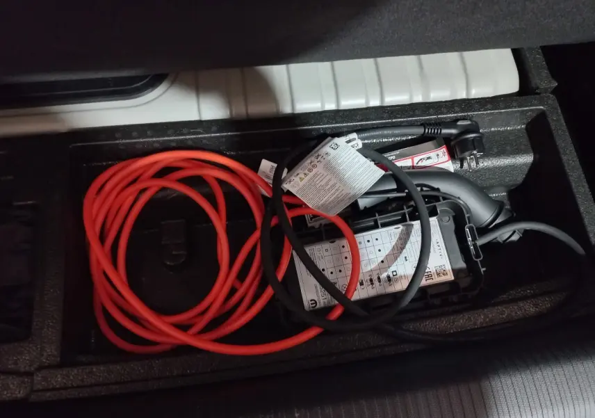 Câbles de recharge rouge et noir rangés dans le coffre d'une Peugeot 308 PHEV 180 E-EAT8 Allure gris foncé.