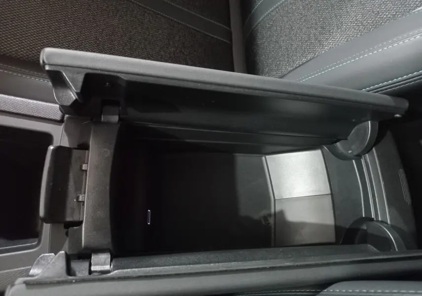 Vue rapprochée de la console centrale ouverte de la Peugeot 308 PHEV 180 Allure, intérieur gris foncé avec surpiqûres bleues.