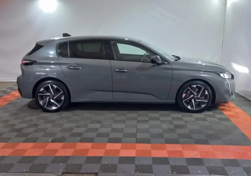 Peugeot 308 PHEV 180 E-EAT8 Allure gris foncé vue de profil côté gauche en intérieur sur sol à damiers noir et orange.