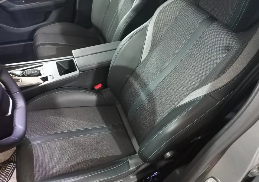 Vue intérieure côté conducteur de la Peugeot 308 PHEV 180 Allure 2025, siège tissu et cuir gris foncé avec console centrale.