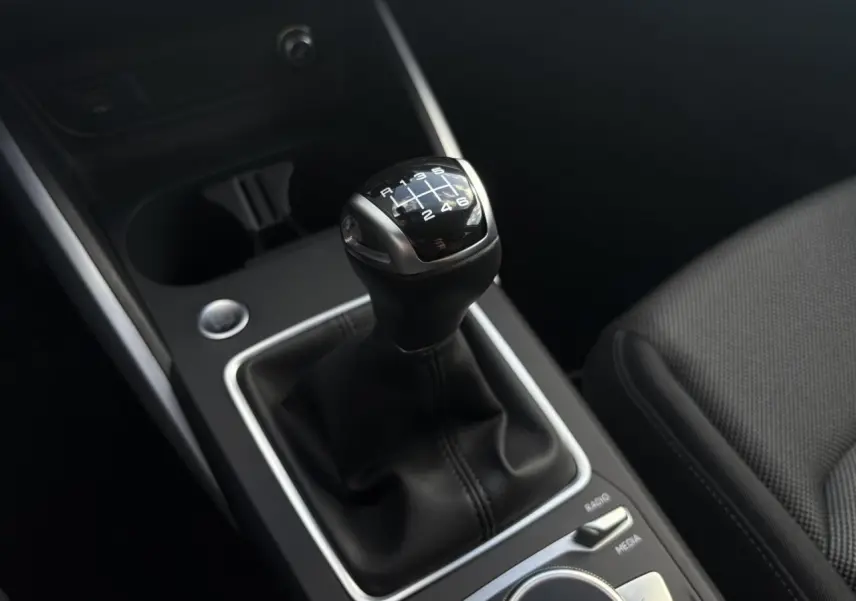 Gros plan sur le levier de vitesses manuel noir de l'Audi Q2 30 TFSI S-Line, avec console centrale et siège en tissu visible.