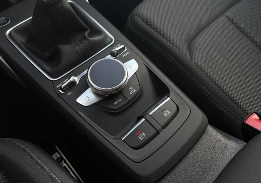 Gros plan sur la console centrale noire de l’Audi Q2 30 TFSI S-Line 2024 avec molette de commande et levier de vitesses manuel.