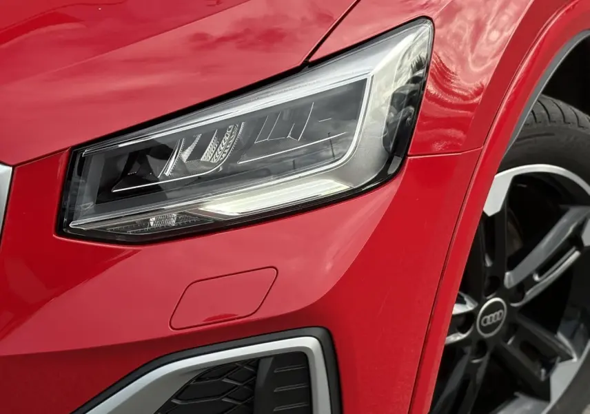 Gros plan sur le phare avant droit et la jante alliage noir poli du SUV Audi Q2 rouge Progressif.
