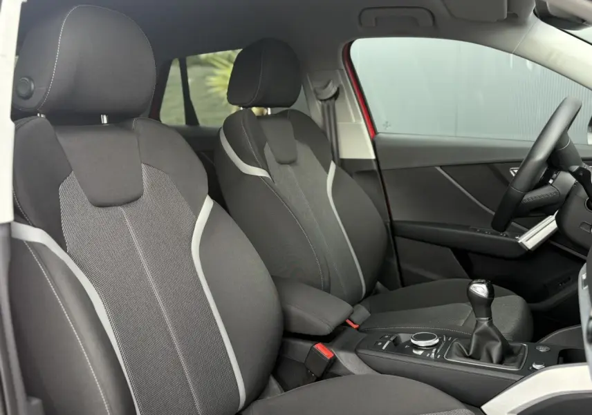 Vue intérieure côté droit de l'Audi Q2 30 TFSI S-Line 2024, sièges sport tissu gris avec surpiqûres claires et levier de vitesses manuel.