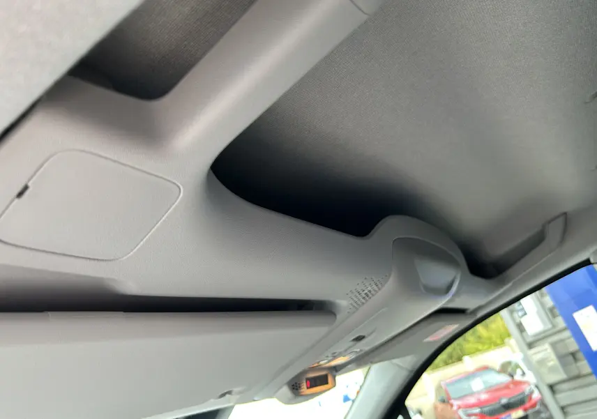 Détail du pare-soleil et plafonnier gris clair à l'intérieur du Peugeot Partner Fourgon blanc visible par la vitre côté droit.