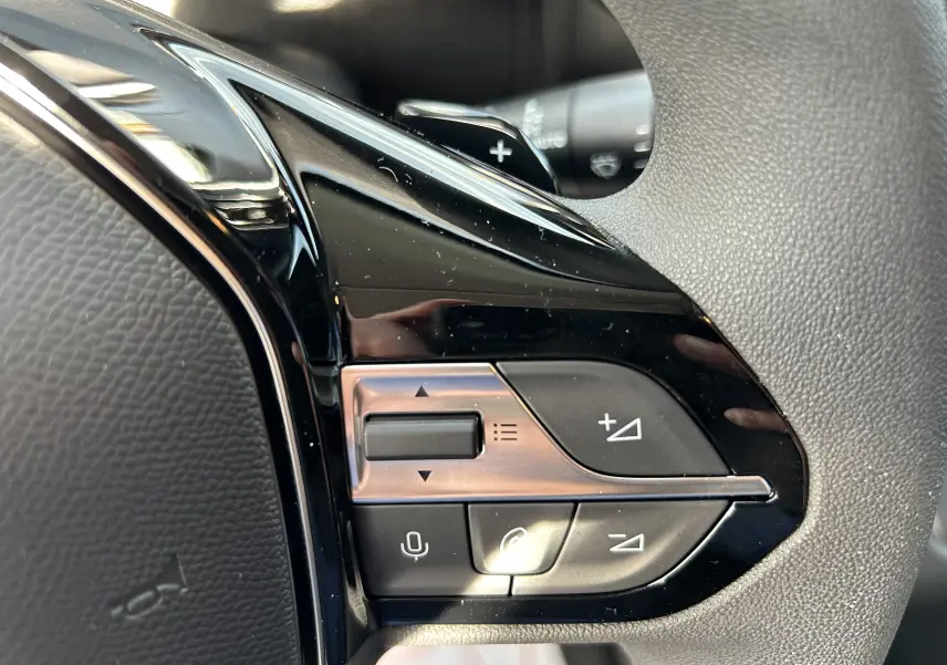 Gros plan sur les commandes multifonctions noires du volant du Peugeot Partner Fourgon blanc, avec boutons de volume et appel.