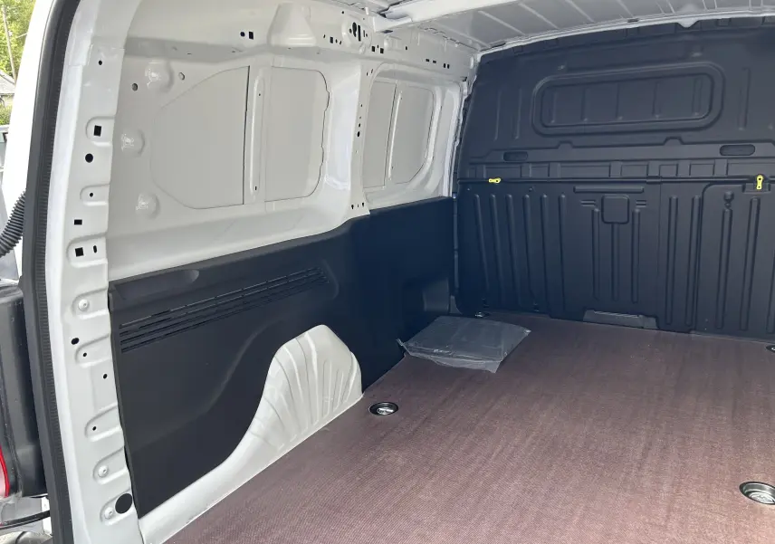 Intérieur du fourgon Peugeot Partner blanc, vue de la zone de chargement avec plancher bois et parois noires.