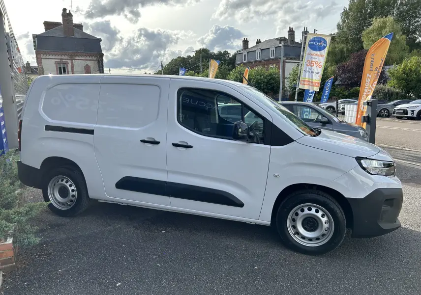 Profil côté droit d'un Peugeot Partner Fourgon blanc 2025 avec protections noires et jantes acier en extérieur urbain.