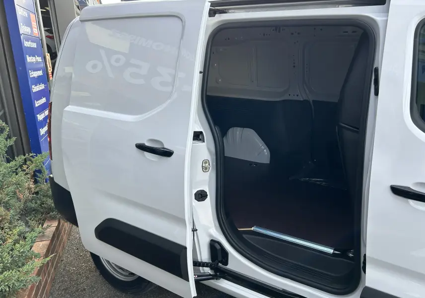 Vue de profil droit du Peugeot Partner Fourgon blanc avec porte latérale ouverte dévoilant le plancher bois intérieur.