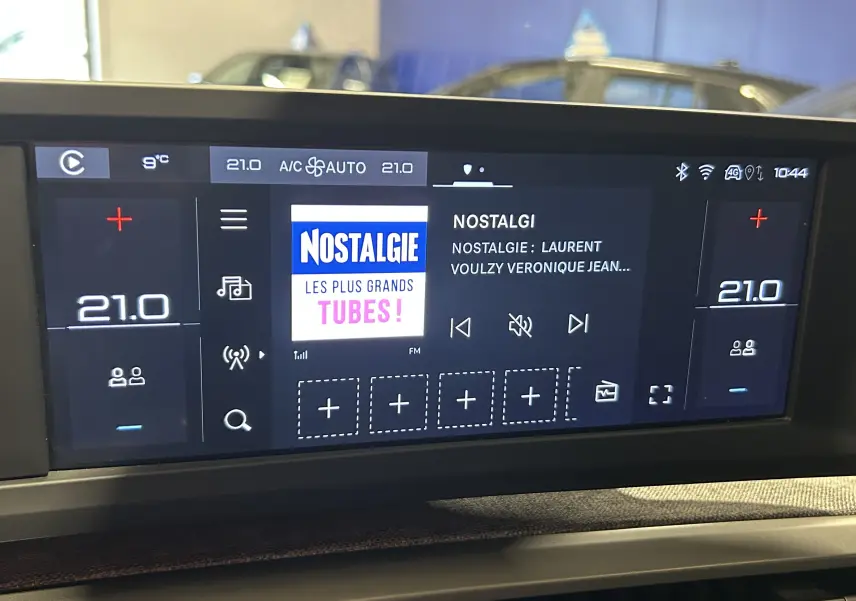 Écran tactile central du Peugeot 5008 hybride 2025 affichant la radio Nostalgie et la climatisation à 21°C.