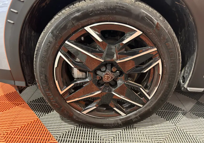 Gros plan sur la jante avant gauche noire et argentée du Peugeot 5008 gris Artense, avec logo lion central visible.