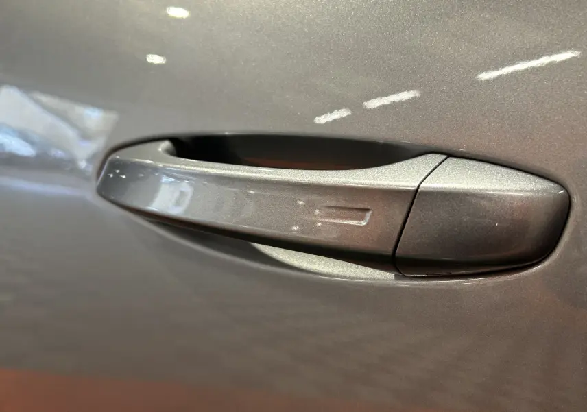 Poignée de porte gris Artense en gros plan sur Peugeot 5008 III Hybrid 145 e-DCS6 Allure, finition métallique brillante.