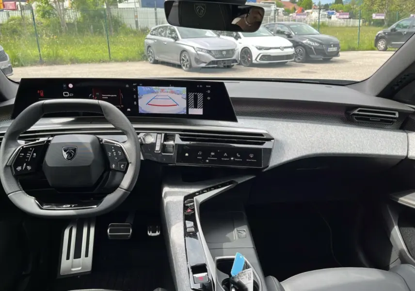 Vue intérieure avant du Peugeot 3008 New Hybrid gris titane, tableau de bord moderne avec écran de recul et volant cuir multifonctions.