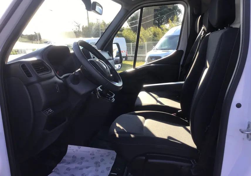 Vue intérieure côté conducteur du Renault Master blanc 2022, montrant les sièges noirs et le tableau de bord simple.