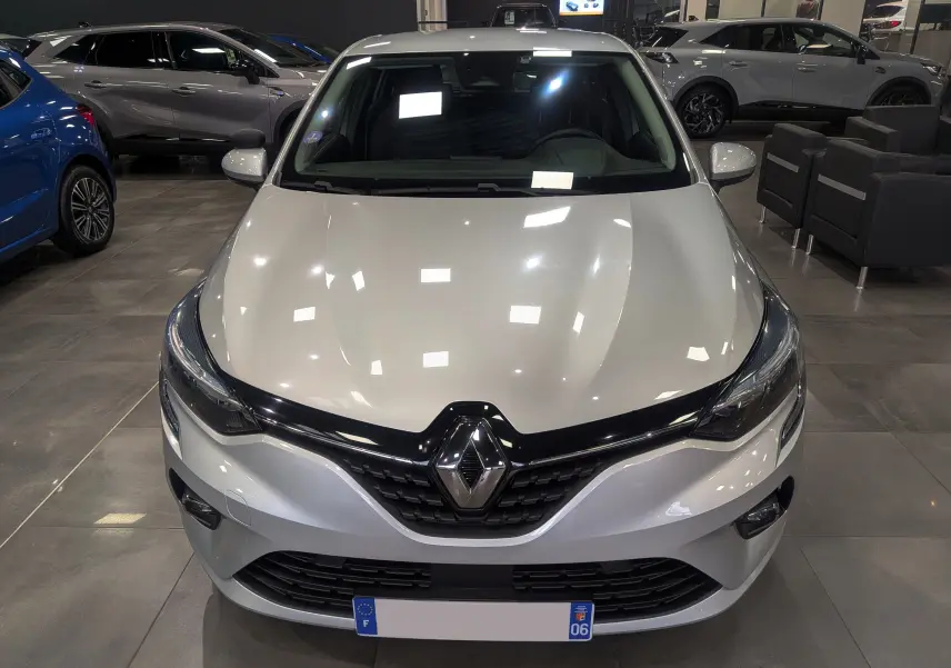 Vue avant d'une Renault Clio V gris platine en showroom, avec calandre noire et logo Renault bien visible.