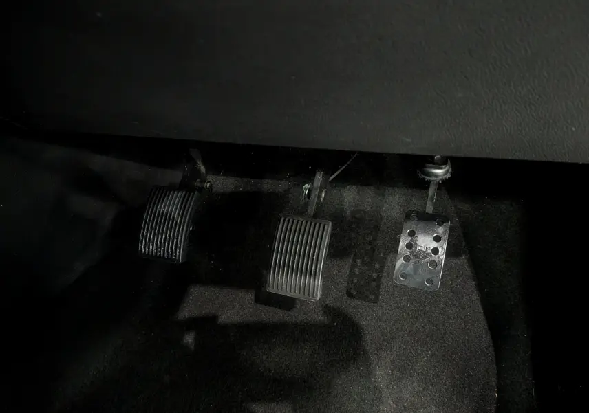 Gros plan sur les trois pédales en métal et caoutchouc de la Renault Clio V gris platine, côté conducteur, boîte manuelle.