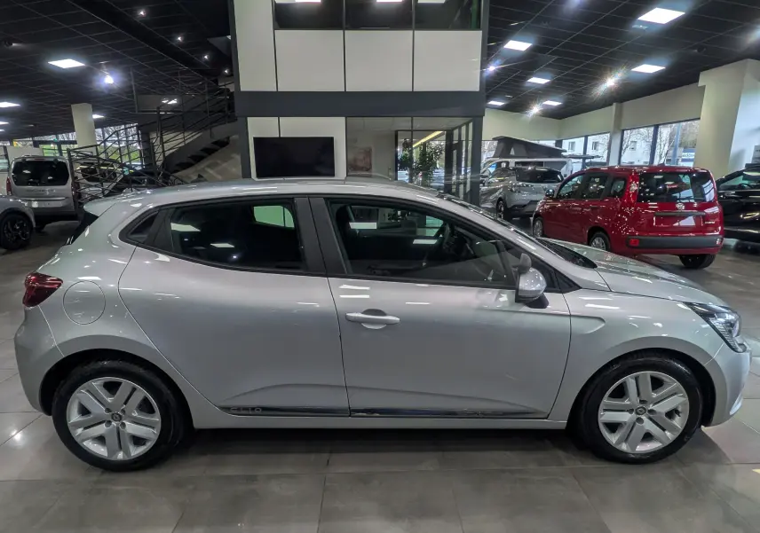 Profil côté gauche d'une Renault Clio V gris platine en intérieur, avec jantes alliage et lignes épurées visibles.