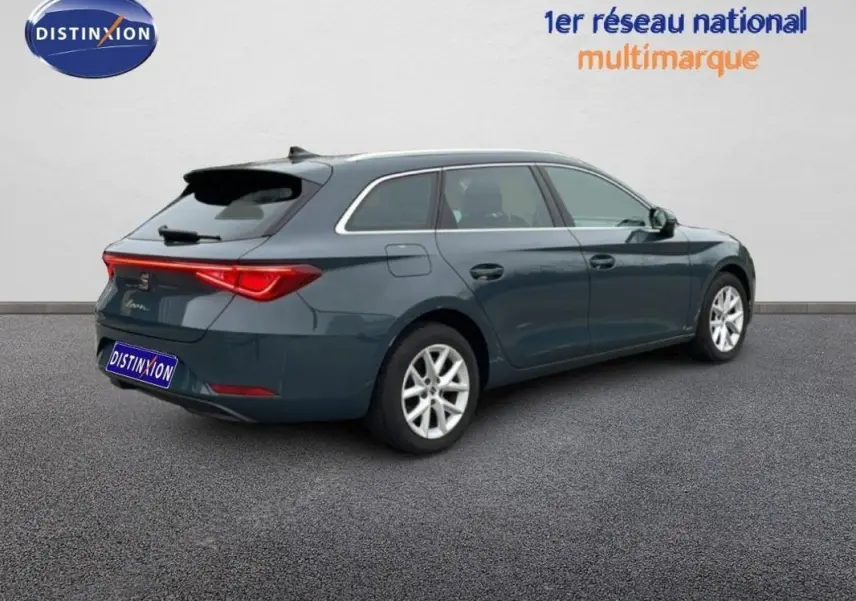 Vue 3/4 arrière droite d'une SEAT Leon ST bleu avec barres de toit et jantes aluminium sur fond neutre.